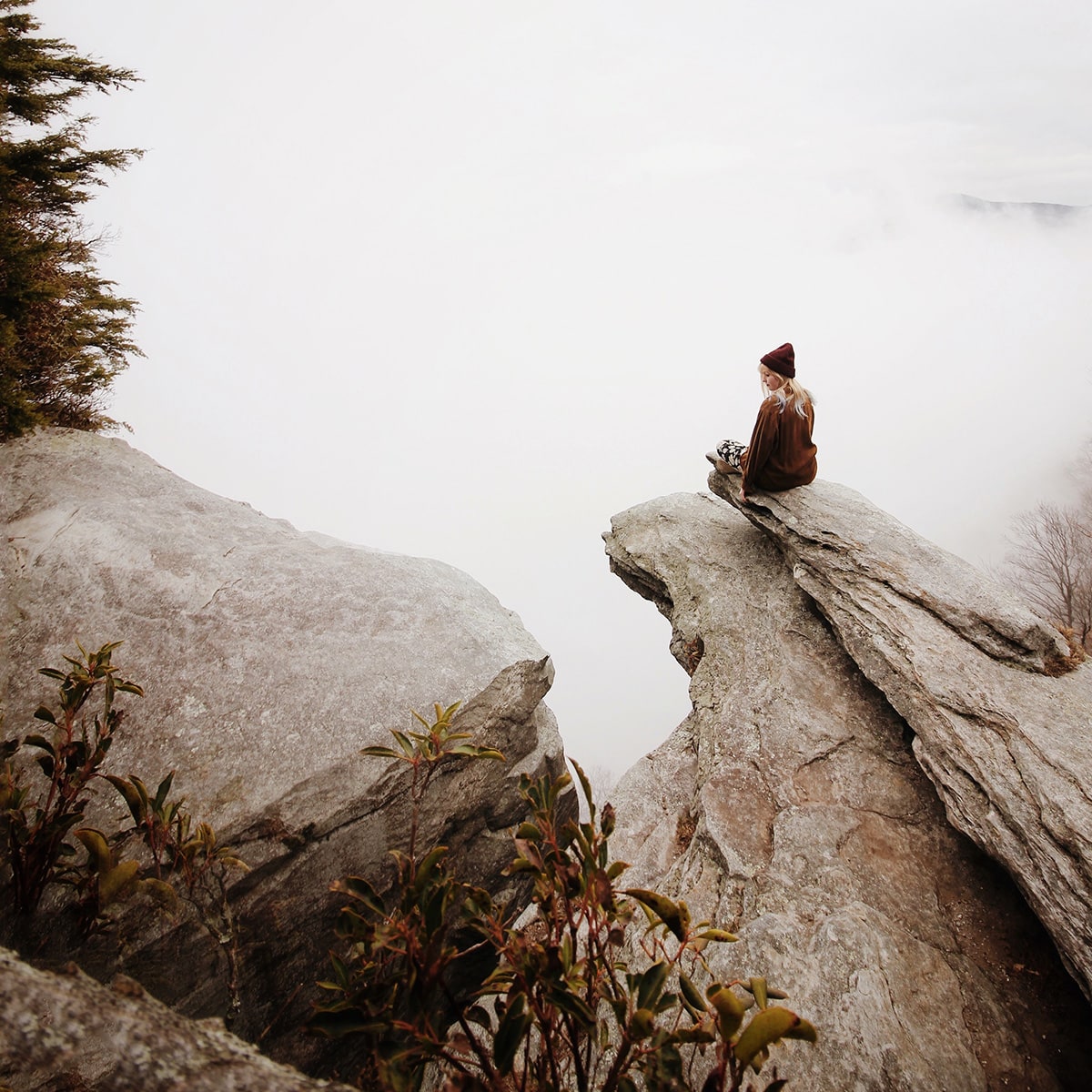 woman sitting on rock outcropping overlooking foggy landscape