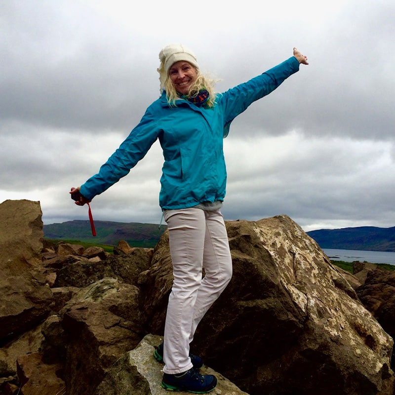 happy woman with outstretched arms standing on boulders overlooking bay