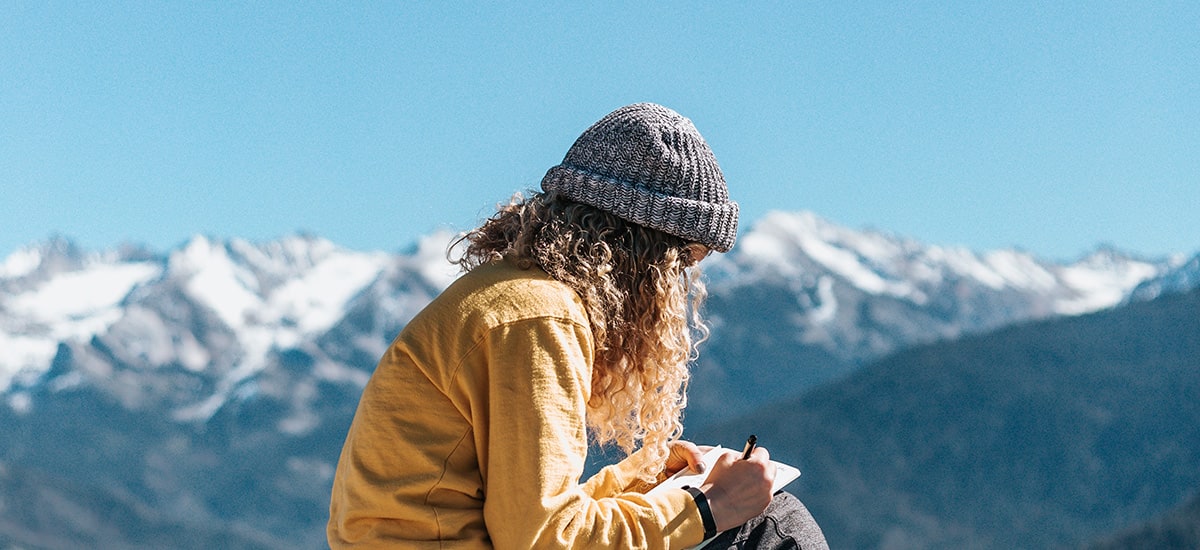 woman writing in journal overlooking mountain range